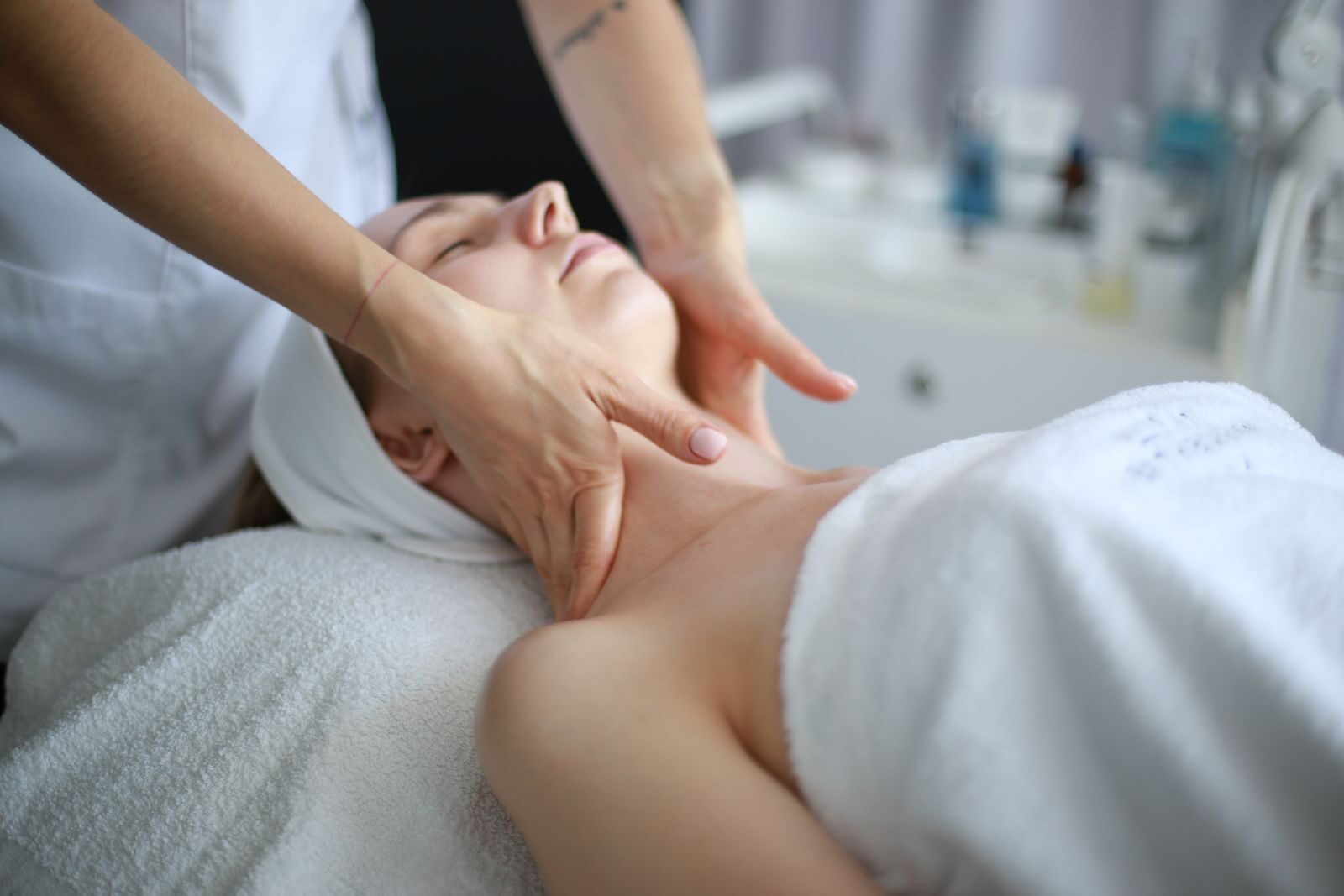 A therapist's hands massaging the side of a woman's neck and jaw