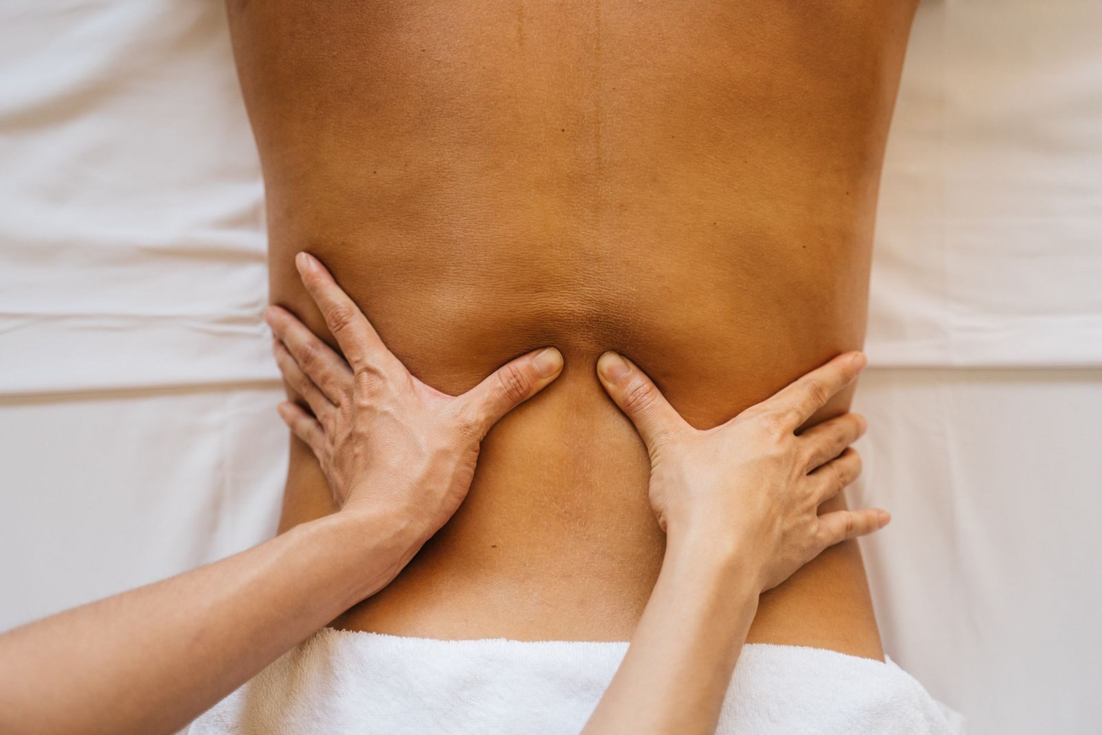 A therapist's hands pressing slowly into the muscles of a person's lower back