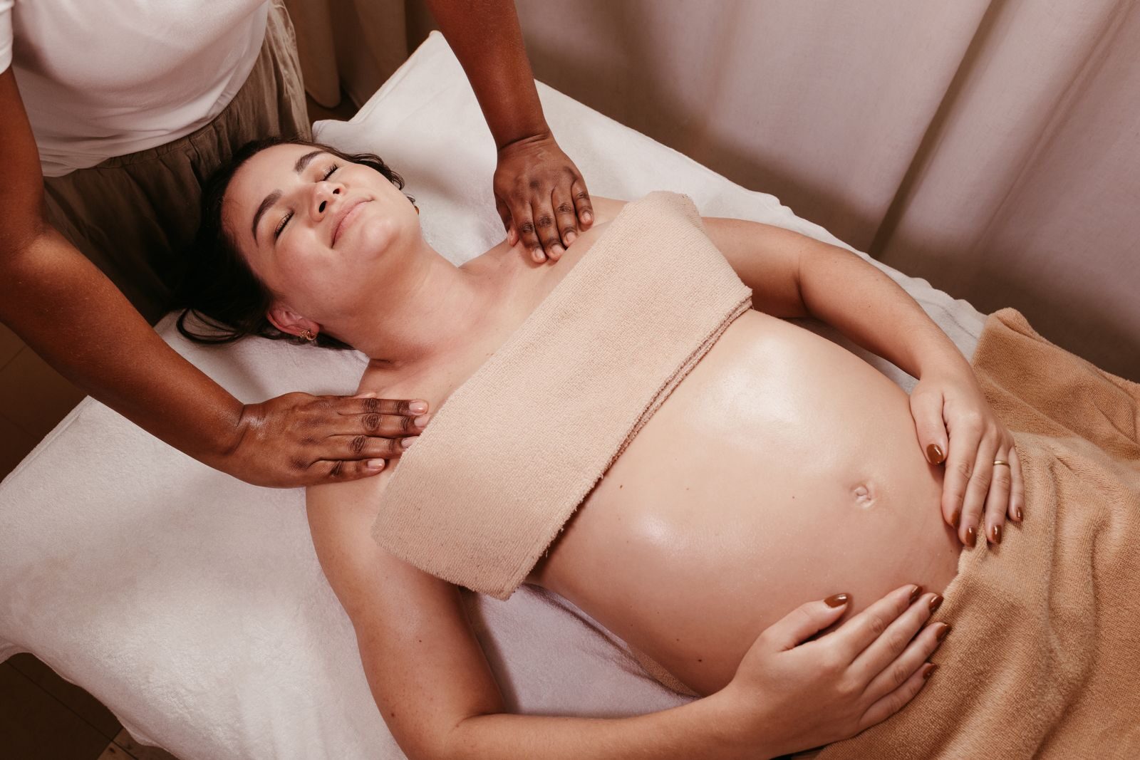 A pregnant woman lying on a massage table while a therapist massages her shoulders